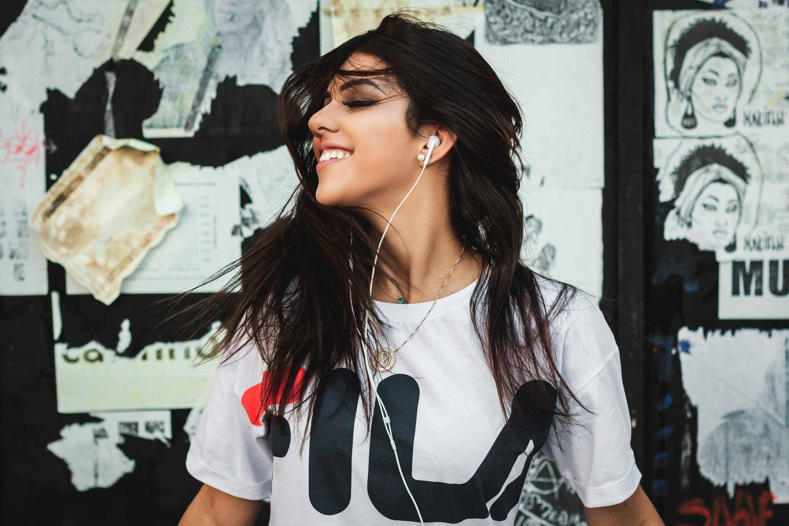 A young woman with long dark hair is wearing headphones and smiling, enjoying the music