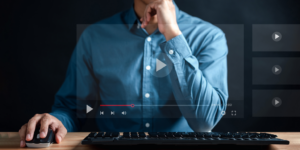 Someone contemplating at their computer. The screen is transparent, and we can see the play features for YouTube on the screen.