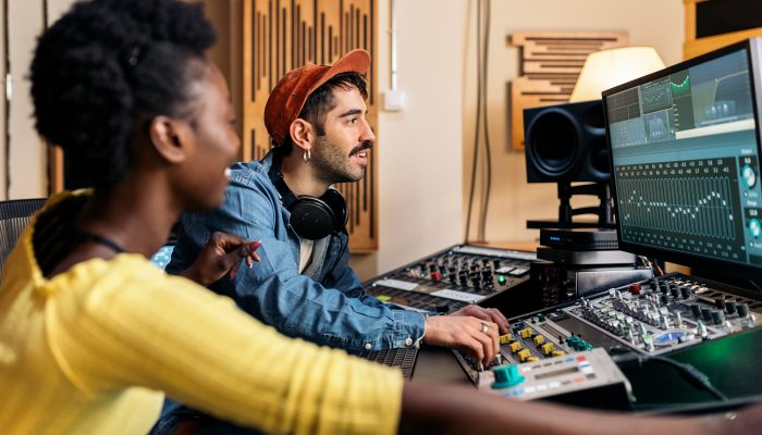 photo of happy Black singer working in professional music studio with young music producer